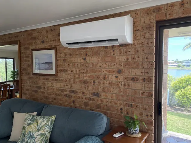 Clean white split-system head on a brick wall in a living room with couch and glass door in Burleigh Waters