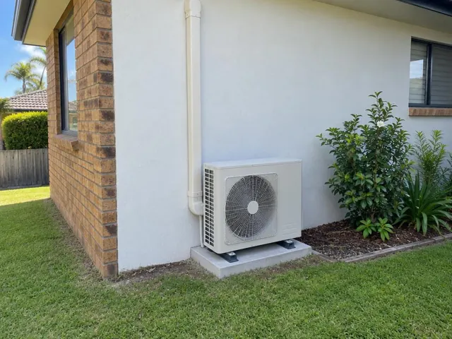 Outdoor air conditioner unit on a concrete pad beside a brick and rendered house wall in Mermaid Waters