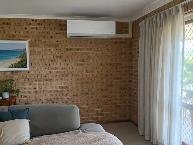 Split system indoor unit mounted high on a brick wall in a living room with curtains in Miami